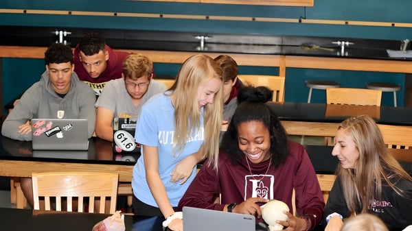 Eine Gruppe von Schülerinnen und Schülern der Pacific Lutheran High School arbeitet zusammen in einem Loungebereich mit Holzmoebeln und türkisfarbener Wand.