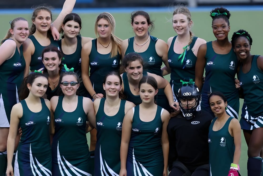 Eine Gruppe junger Sportlerinnen in einheitlichen grünen und schwarzen Trikots steht auf dem Sportplatz des Pakuranga College.