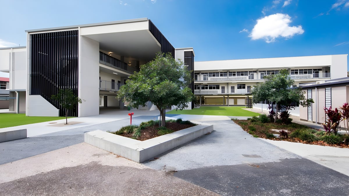 Das moderne mehrstöckige Schulgebäude der Palm Beach Currumbin State High School ist von grünen Bäumen umgeben.