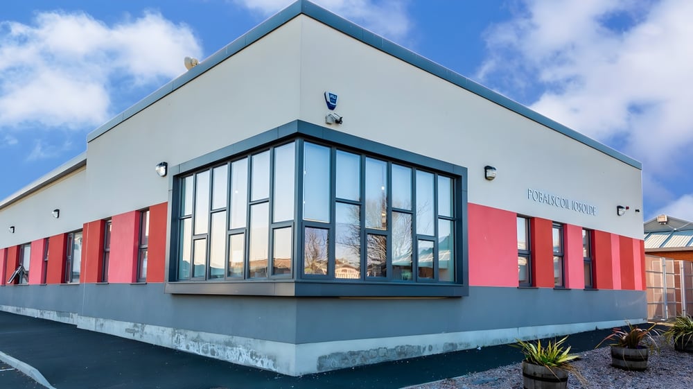 Das moderne Gebäude der Palmerstown Community School mit großen Glasfenstern vor einem blauen Himmel mit weißen Wolken.