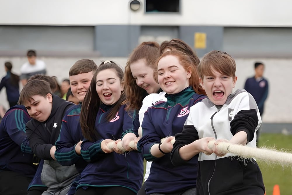 Schüler der Palmerstown Community School feiern gemeinsam auf einem Sportfeld vor einem Schulgebäude.