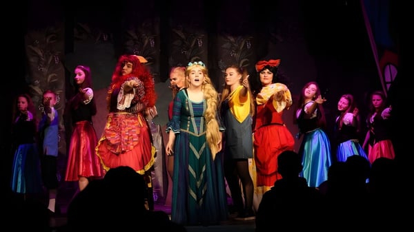 Frauen in bunten Kostümen stehen auf der Bühne der Palmerstown Community School bei einem Bühnenauftritt.