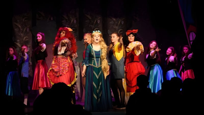 Frauen in bunten Kostümen stehen auf der Bühne der Palmerstown Community School bei einem Bühnenauftritt.