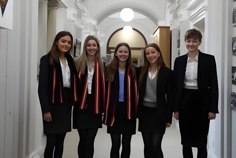Fünf Jugendliche in formeller Kleidung stehen gemeinsam im Flur auf dem Campus des Pangbourne College.