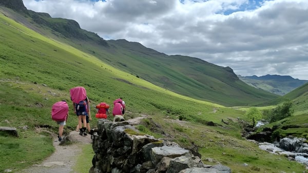 Eine Gruppe von Schülerinnen und Schülern des Pangbourne College wandert auf einem felsigen Pfad in einer grünen Berglandschaft.