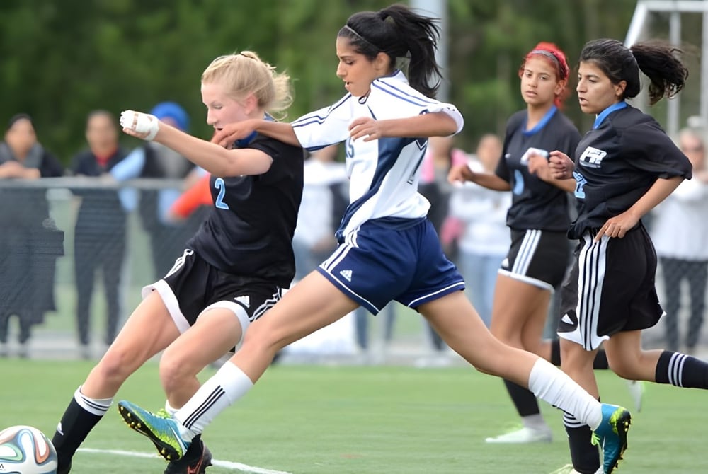Schülerinnen der Panorama Ridge Secondary School spielen Fußball auf einem Spielfeld vor einem Sportgebäude.