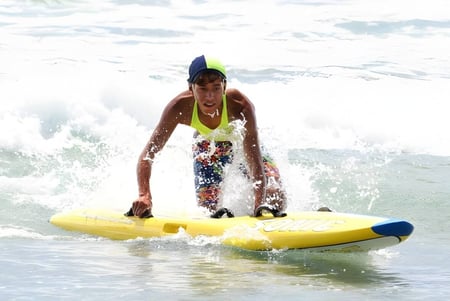 Eine Person auf einem gelben Surfbrett fährt durch die Wellen vor der Küste des Papamoa College.