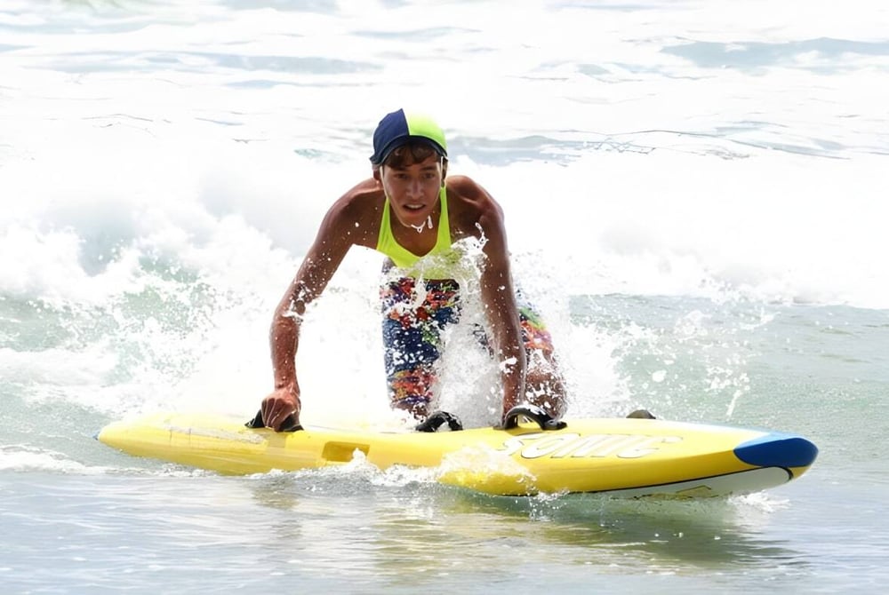 Eine Person auf einem gelben Surfbrett fährt durch die Wellen vor der Küste des Papamoa College.