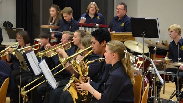 Eine Gruppe von Musikern der Papanui High School in dunkelblauen Uniformen spielt auf einer Bühne verschiedene Blas- und Holzblasinstrumente.