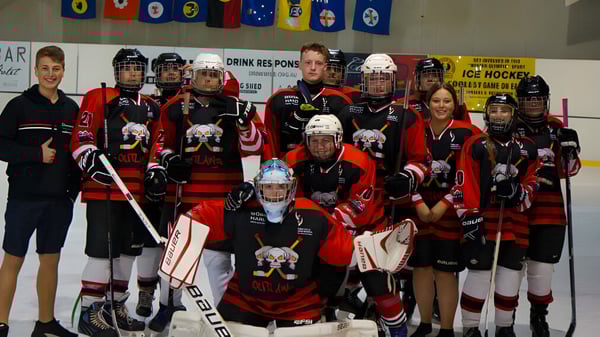 Eine Gruppe von Hockey-Schülern der Para Hills High School posiert in einer Eishalle mit Mannschaftsbannern im Hintergrund.