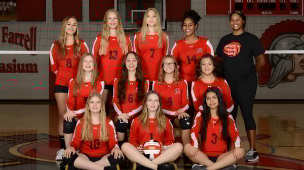 Eine Gruppe junger Volleyballspielerinnen in roten Trikots im Paradise Valley Unified School District posiert in der Turnhalle.