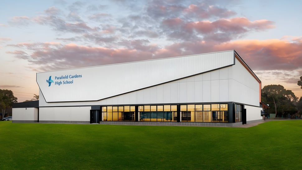 Das moderne weiße Gebäude der Parafield Gardens High School steht vor einem grünen Feld unter einem dramatischen Sonnenuntergangshimmel.