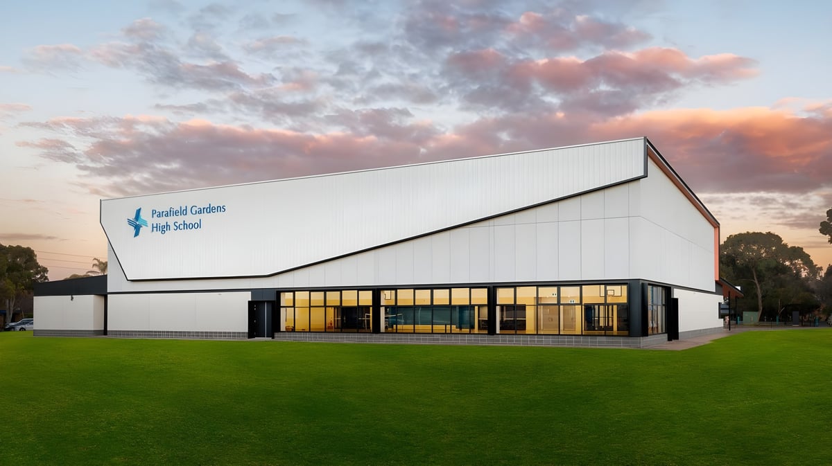 Das moderne weiße Gebäude der Parafield Gardens High School steht vor einem grünen Feld unter einem dramatischen Sonnenuntergangshimmel.