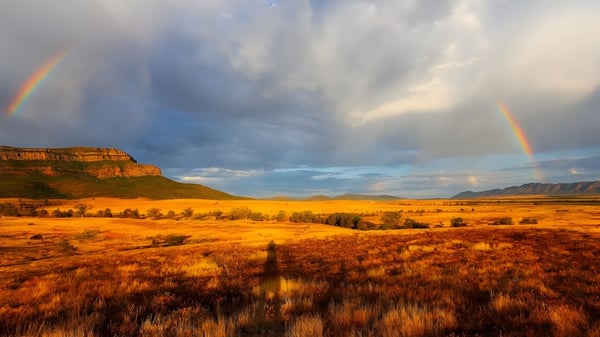 Ein weites, goldenes Feld mit Regenbögen und dramatischem Himmel bei Paralowie R-12 School in der Ferne.