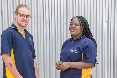 Zwei Personen in Uniformen stehen vor einer Wellblechwand auf dem Gelände der Paralowie R-12 School.