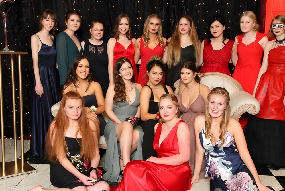 Eine Gruppe von Schülerinnen des Paraparaumu College posiert in formellen Kleidern vor einem dunklen Hintergrund mit funkelnden Lichtern.