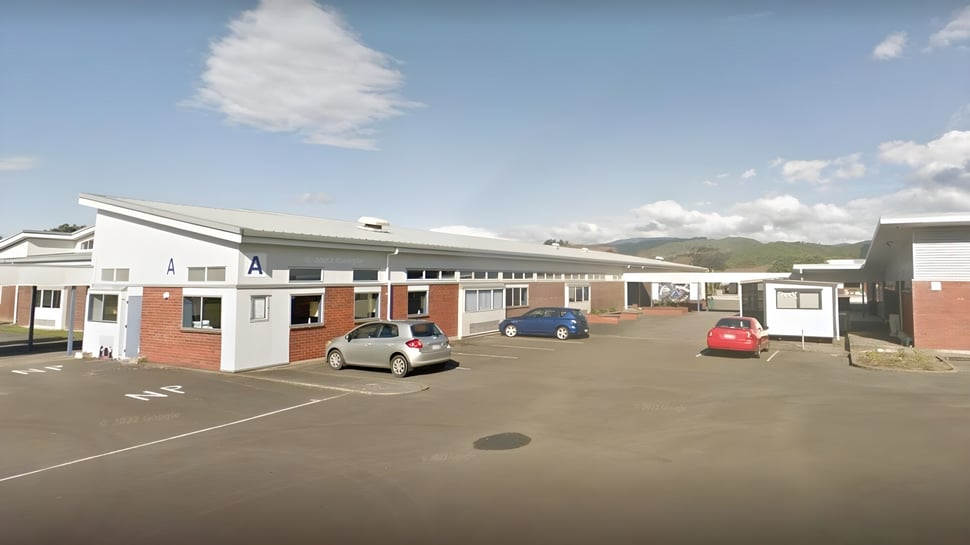 Das einstöckige Schulgebäude von Paraparaumu College mit Parkplatz und hügeliger Landschaft im Hintergrund.