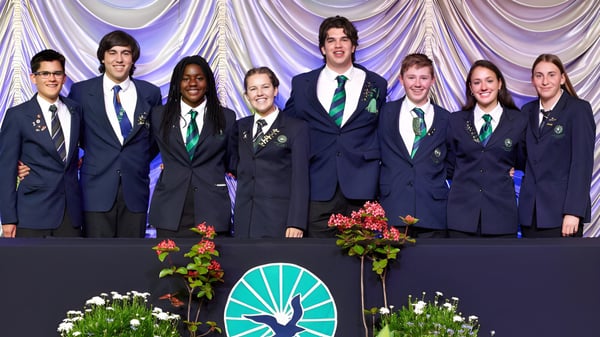 Schüler des Paraparaumu College stehen in Schuluniformen auf einer Bühne mit Blumenarrangement und Vorhang im Hintergrund.
