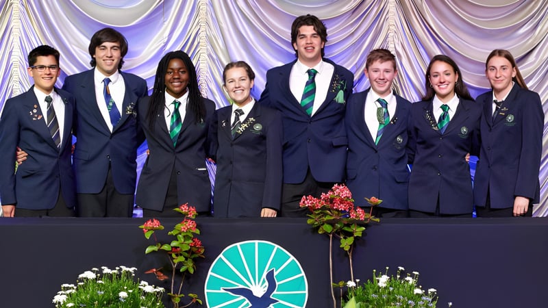 Schüler des Paraparaumu College stehen in Schuluniformen auf einer Bühne mit Blumenarrangement und Vorhang im Hintergrund.