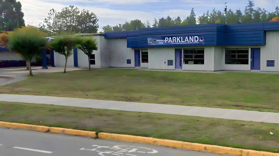 Das moderne blaue Gebäude der Parkland Secondary School steht umgeben von einer Grünfläche und Bäumen.