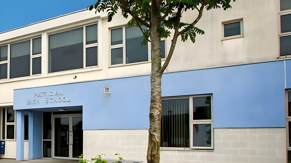 Das moderne zweistöckige Gebäude der Patrician High School mit großen Fenstern und einem Baum im Vordergrund bei klarem Himmel.