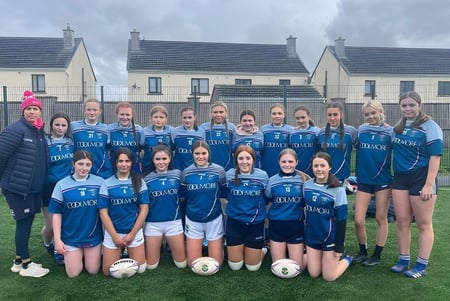 Eine Gruppe junger Fußballspielerinnen der Patrician Presentation Secondary School posiert vor Wohnhäusern unter einem bewölkten Himmel.