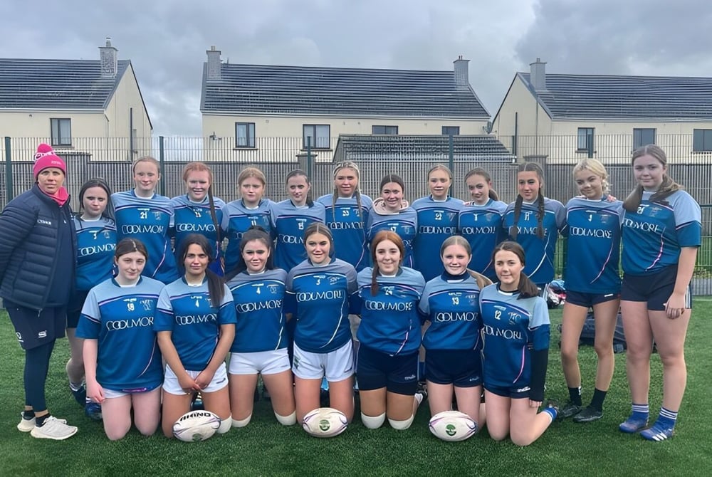 Eine Gruppe junger Fußballspielerinnen der Patrician Presentation Secondary School posiert vor Wohnhäusern unter einem bewölkten Himmel.