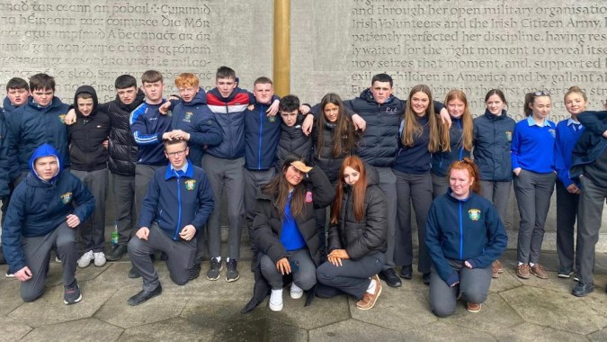 Eine Gruppe von Schülerinnen und Schülern der Patrician Presentation Secondary School steht gemeinsam vor einer Wand mit Text.