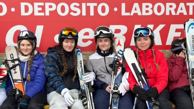 Eine Gruppe von Schülerinnen und Schülern der Patrician Presentation Secondary School steht mit Skiausrüstung vor einem großen Schild.