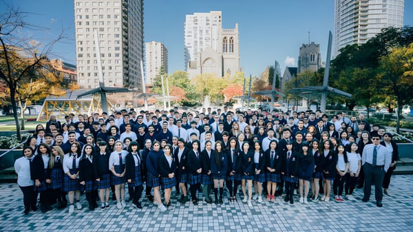 Eine Gruppe von Schülern der Pattison High School versammelt sich vor einer Stadtkulisse mit hohen Gebäuden und einem Kirchturm.