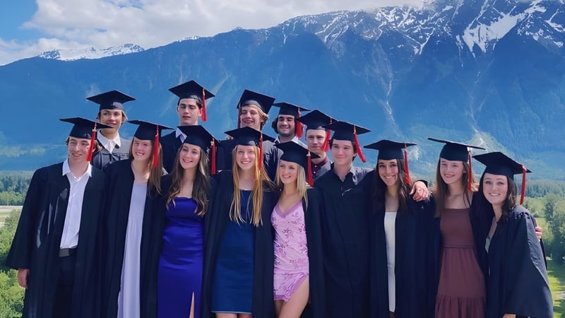 Eine Gruppe Absolventen steht in akademischer Kleidung vor einer Berglandschaft auf dem Gelände der Pemberton Secondary School.
