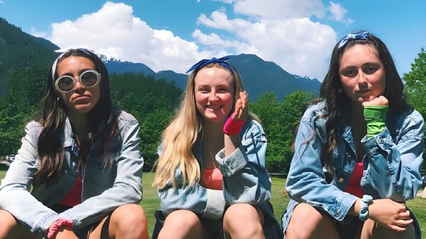 Drei Schülerinnen der Pemberton Secondary School sitzen zusammen im Freien mit Bergen und Wald im Hintergrund.