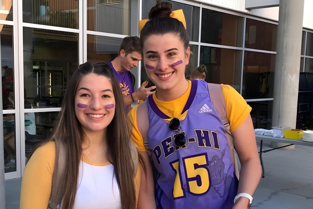 Zwei Schülerinnen der Penticton Secondary School stehen lächelnd vor einem Gebäude mit großen Fenstern.