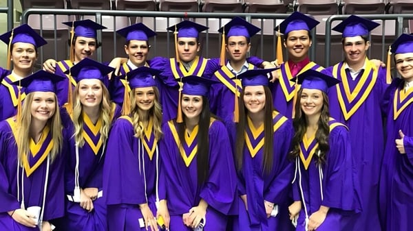 Absolventinnen und Absolventen der Penticton Secondary School stehen in violetten und goldenen Talaren für ein Foto in einem Innenraum.