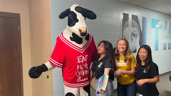 Der Maskottchen der Peoria Christian School steht mit einer Gruppe lächelnder Schülerinnen im Schulflur.