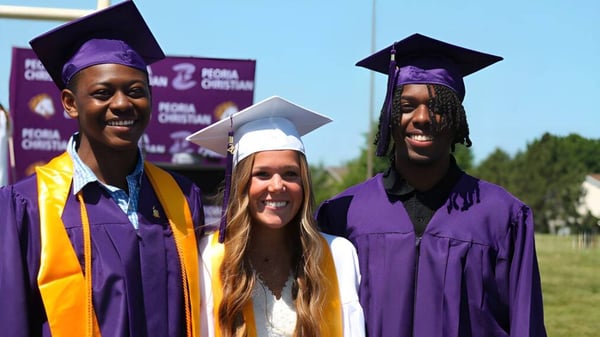 Drei Absolventen in violetten Talaren stehen vor einer Kulisse mit dem Logo der Peoria Christian School.