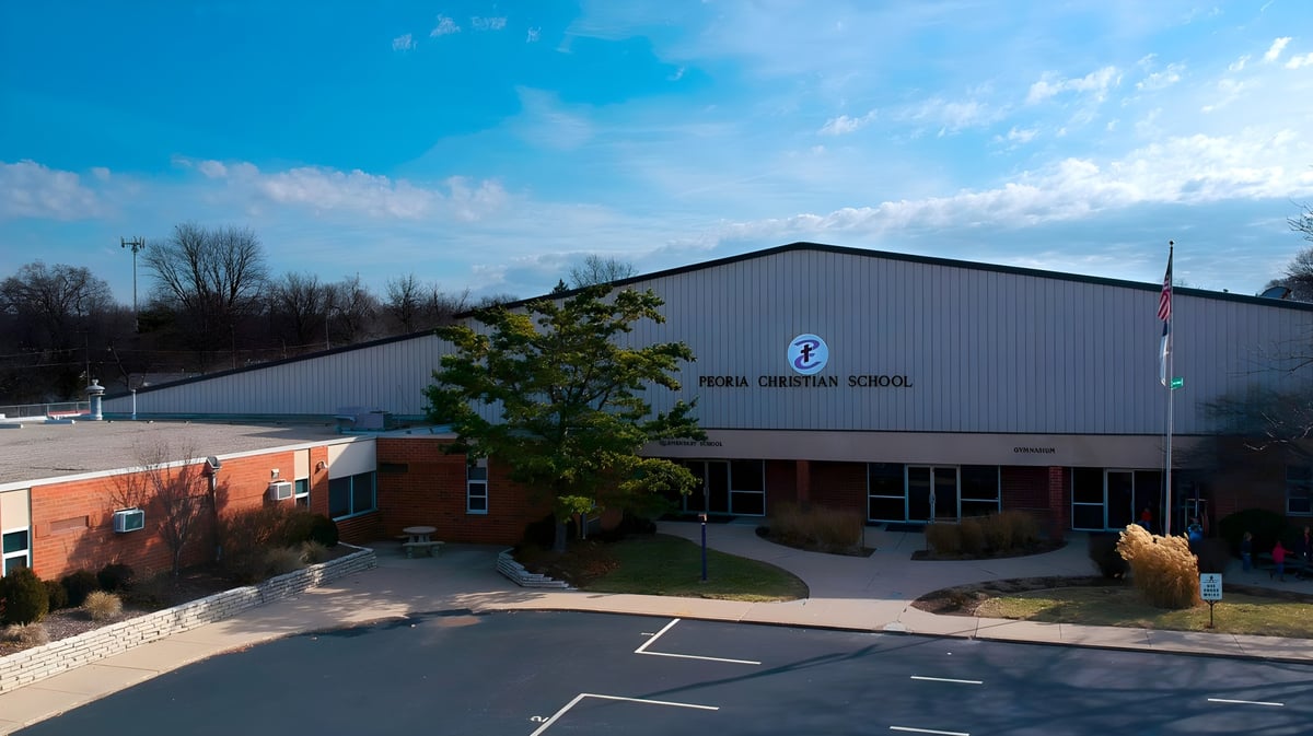 Das moderne Schulgebäude der Peoria Christian School mit großem Parkplatz und Bäumen im Hintergrund.