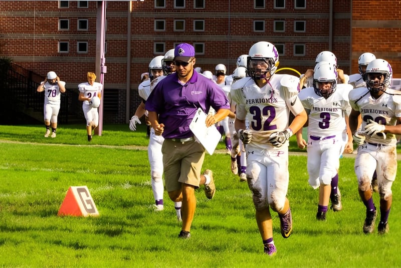 Eine Gruppe von Fußballspielern in Uniform läuft über ein Grasfeld auf dem Campus der Perkiomen School.