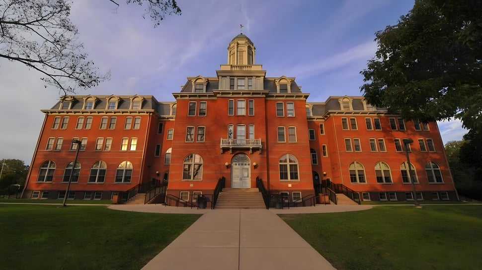 Das historische rote Backsteingebäude der Perkiomen School steht in einer gepflegten Grünanlage mit Bäumen und blauem Himmel.