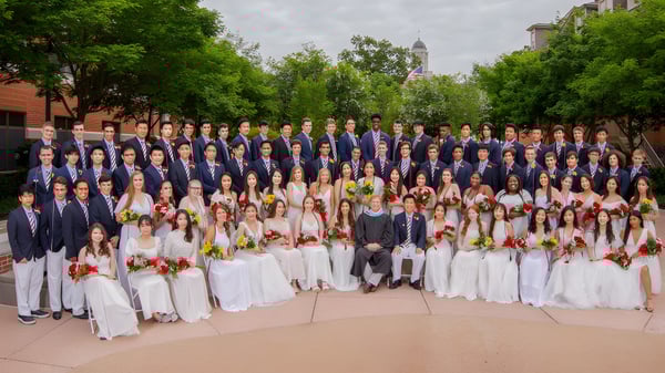 Eine große Gruppe von Menschen in formeller Kleidung versammelt sich draußen vor einem Gebäude mit einem hohen Turm auf dem Campus der Perkiomen School.