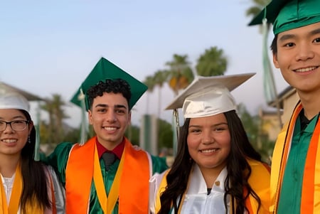 Eine Gruppe von Schülerinnen und Schülern der Phoenix Christian Preparatory School steht in ihren Abschlussroben vor einer malerischen Kulisse mit Palmen.