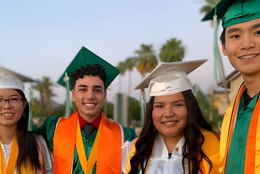 Eine Gruppe von Schülerinnen und Schülern der Phoenix Christian Preparatory School steht in ihren Abschlussroben vor einer malerischen Kulisse mit Palmen.