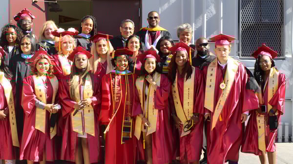 Eine Gruppe von Absolventen der Phoenix Magnet Academy steht in roten und goldenen Roben vor einem Gebäude mit roter und weißer Fassade.