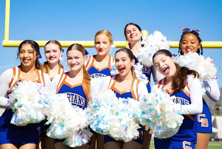 Cheerleader des Phoenix Union High School District stehen mit bunten Pompons vor blauem Himmel und gelbem Torpfosten.