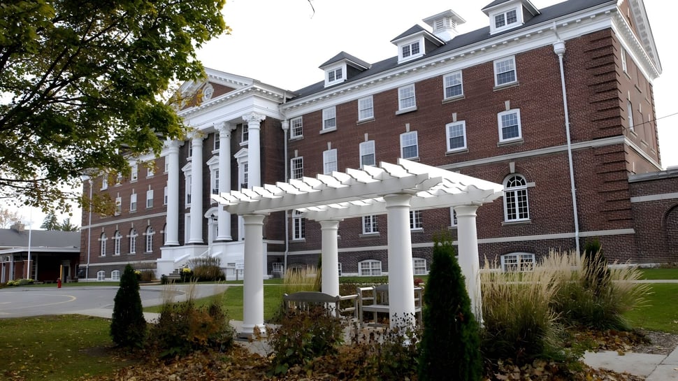 Das Backsteingebäude mit weißer Säulenfassade des Pickering College steht umgeben von Bäumen und Sträuchern.