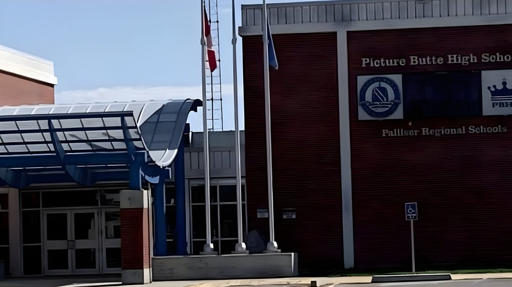Das Backsteingebäude der Picture Butte High School mit markantem Eingang und wehenden Flaggen ist zu sehen.