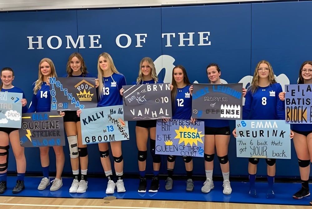 Eine Gruppe weiblicher Volleyballspielerinnen posiert vor einer blauen Wand auf dem Campus der Picture Butte High School.