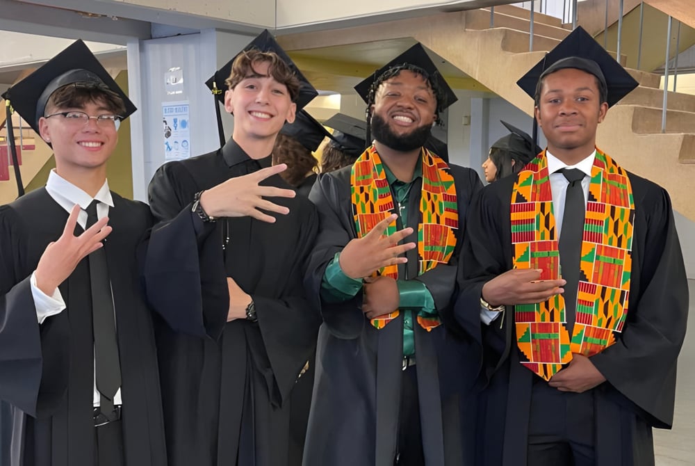 Vier Schüler der Pierrefonds Community High School in Abschlusskleidung posieren gemeinsam für ein Foto im Schulflur.