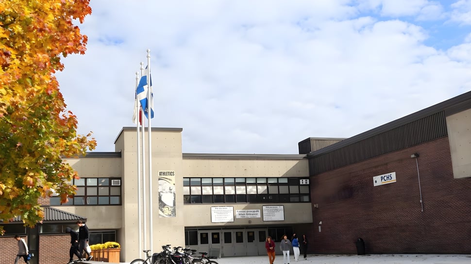 Das Backsteingebäude mit einem hohen Turm der Pierrefonds Community High School ist von Bäumen mit herbstlichem Laub umgeben.