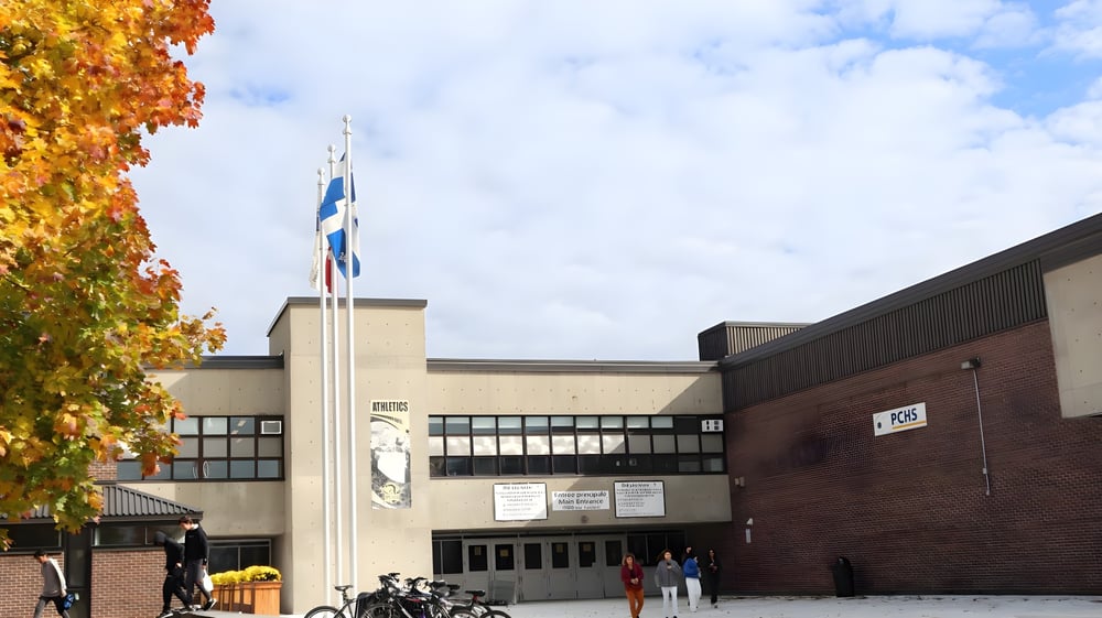 Das Backsteingebäude mit einem hohen Turm der Pierrefonds Community High School ist von Bäumen mit herbstlichem Laub umgeben.